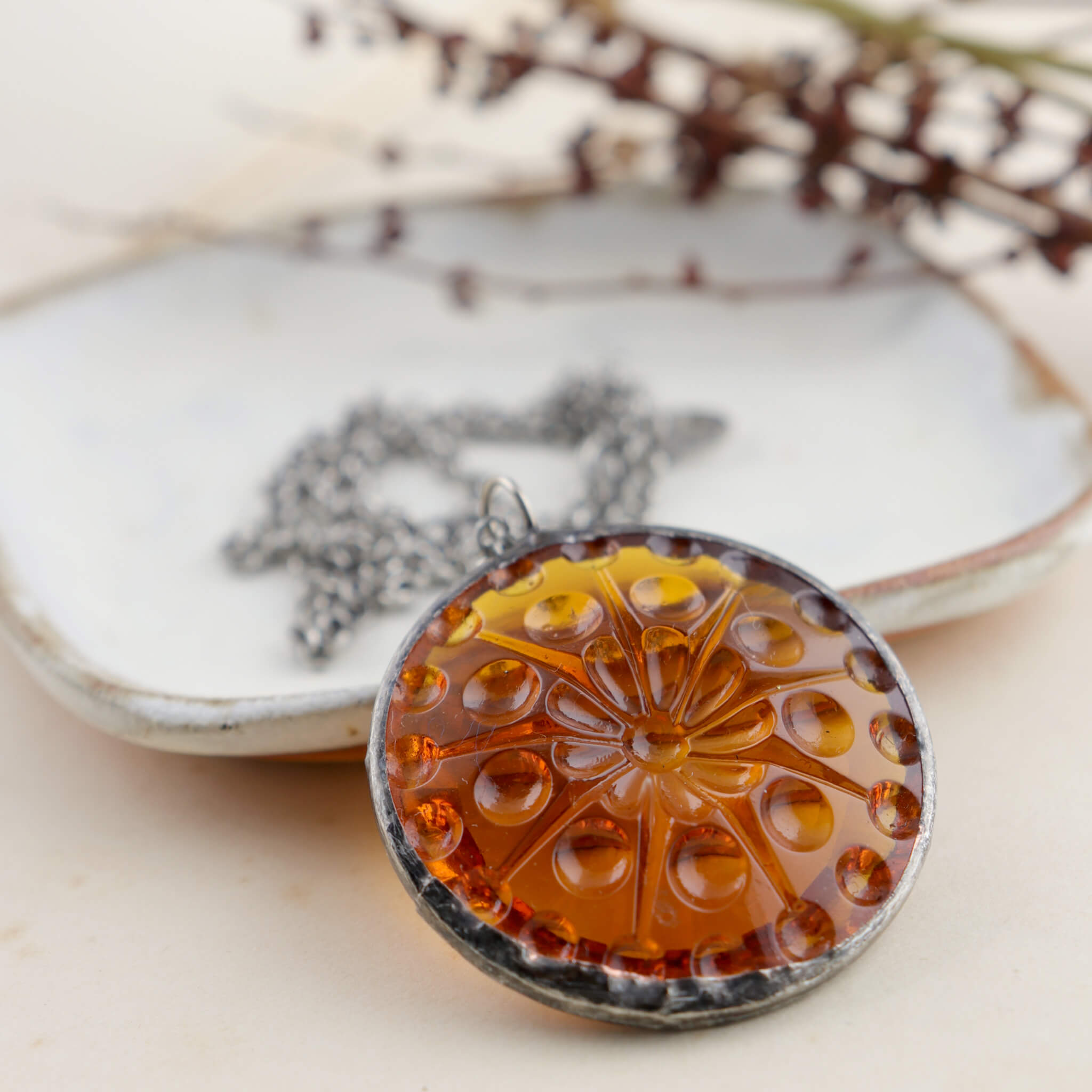 Centric pattern amber glass rondelle framed into stained glass necklace leaning on a white dish