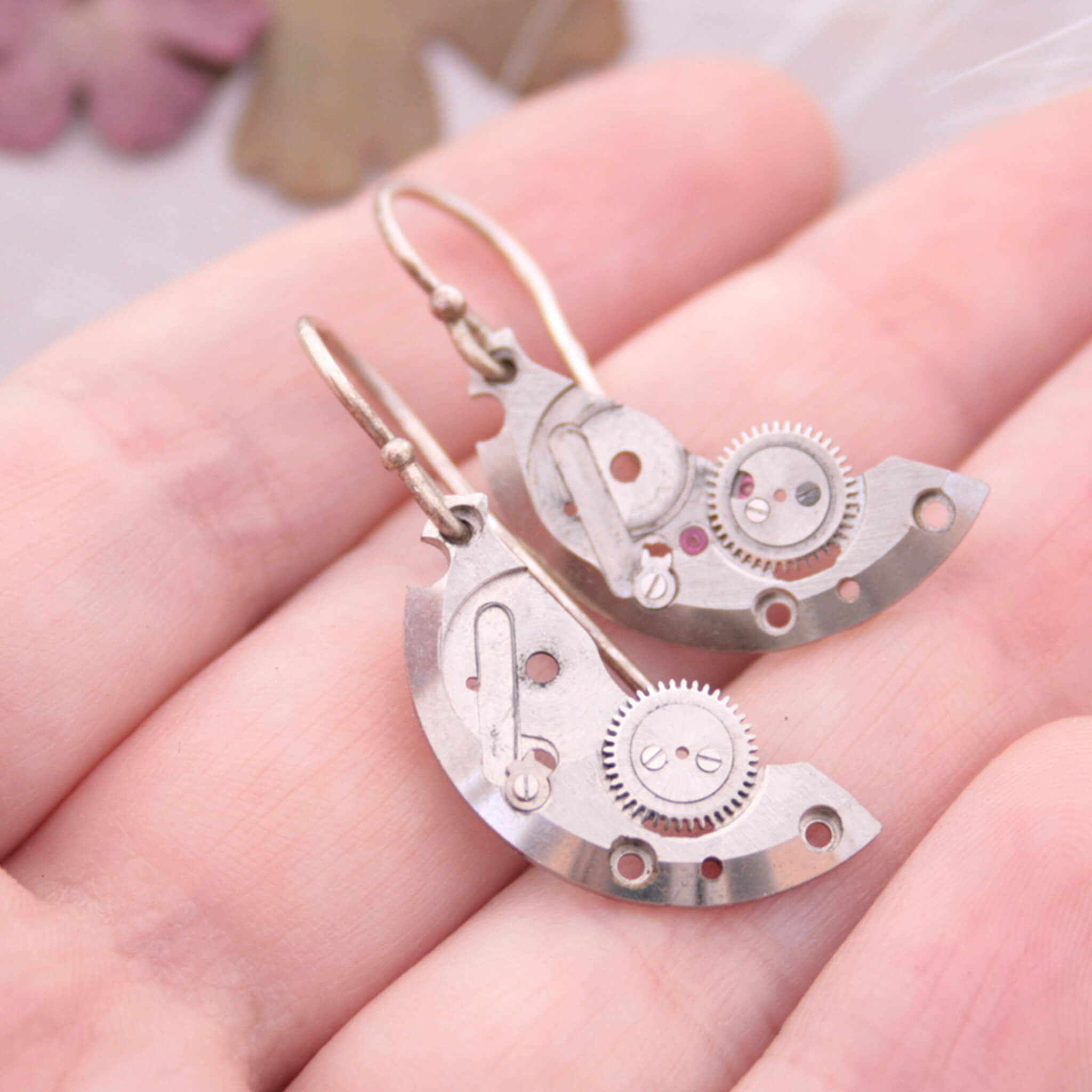 watch parts turned into dangling earrings lying on a hand