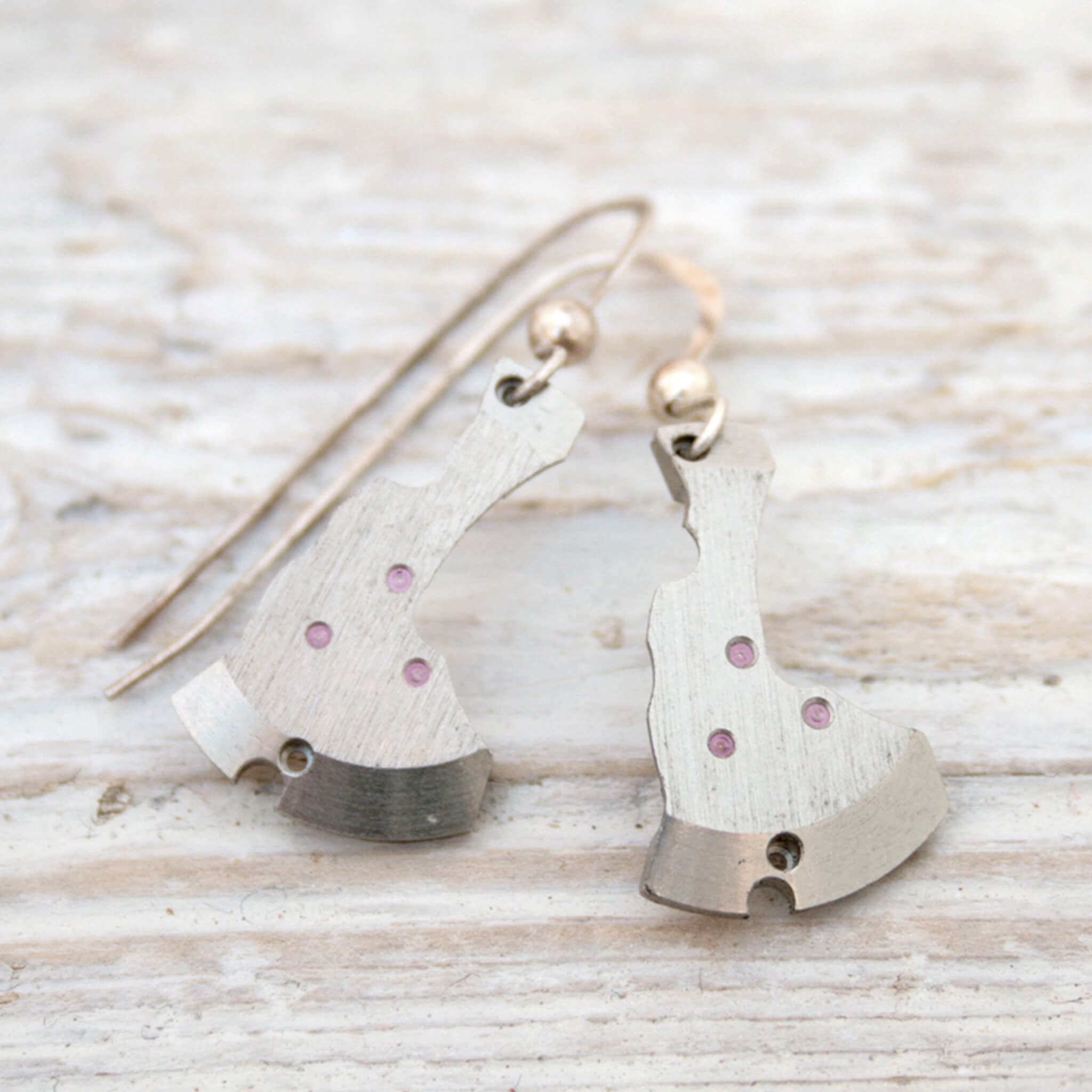watch parts turned into dangling earrings lying on a wood painted white