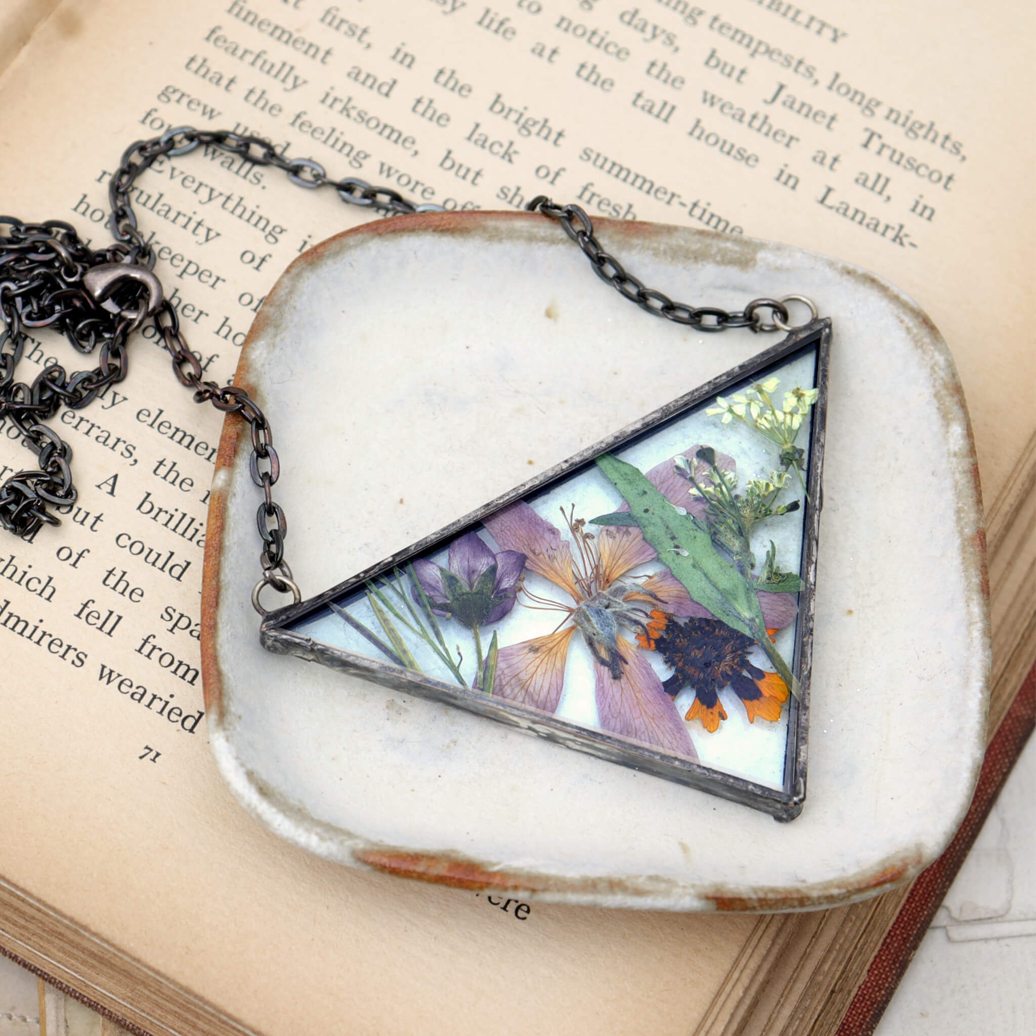 Necklace of a mix of pressed flowers in triangular soldered glass lying on a white dish