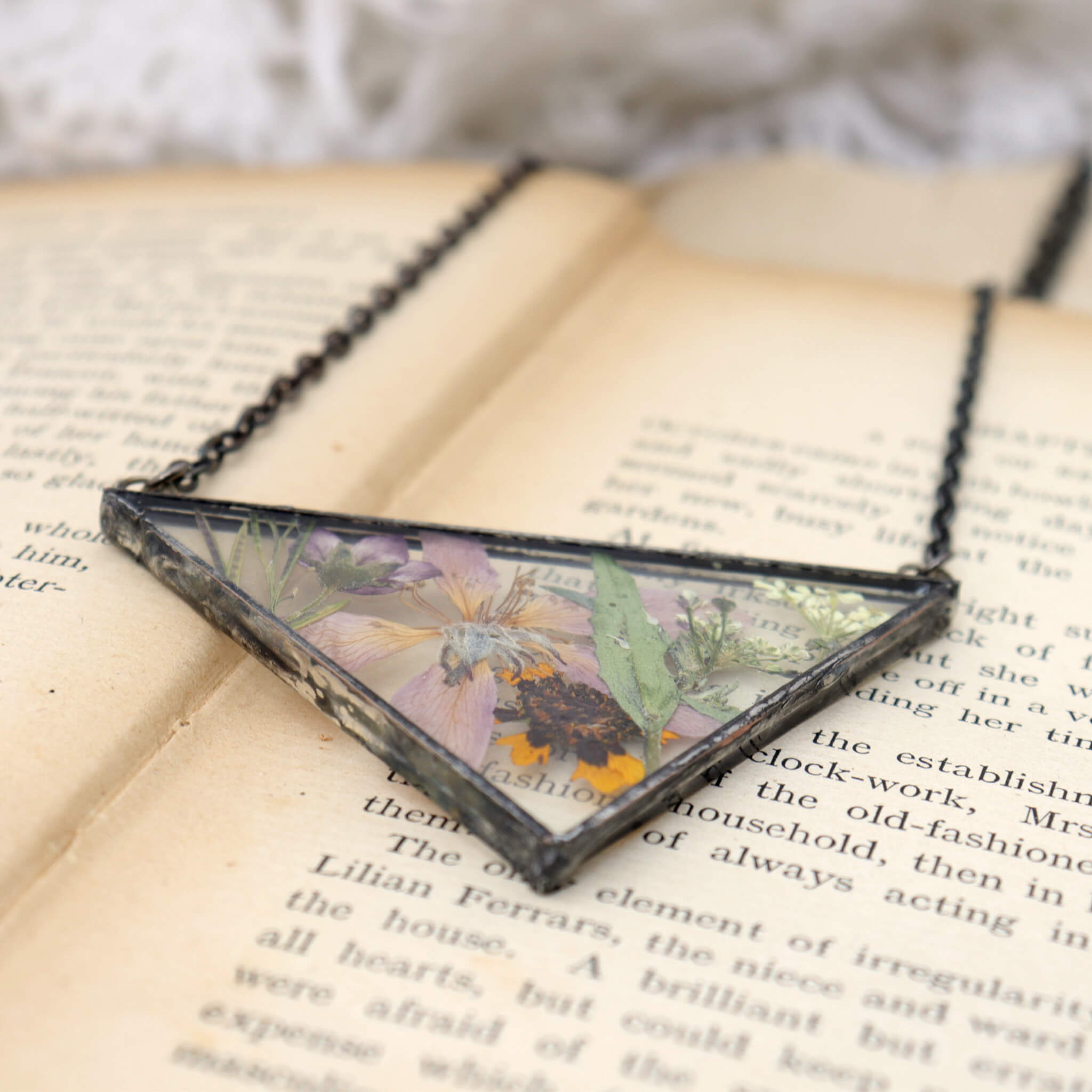 Necklace of a mix of pressed flowers in triangular soldered glass lying on an old book