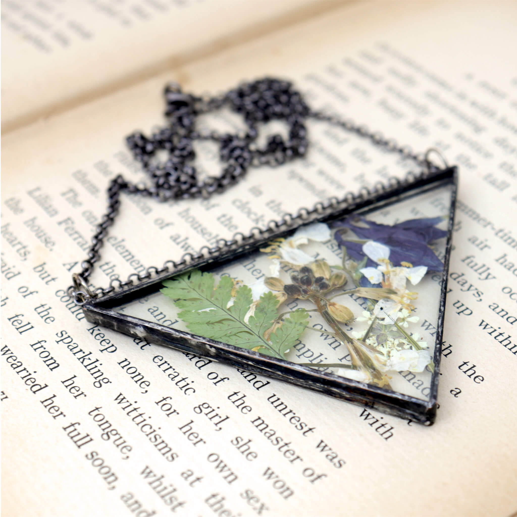 Necklace of a mix of pressed flowers in triangular soldered glass lying on an old book