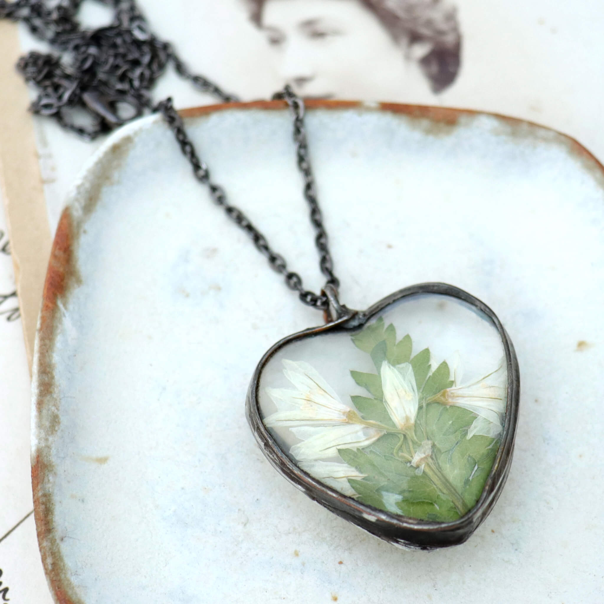 Stained glass style pressed flowers necklace lying on a white dish
