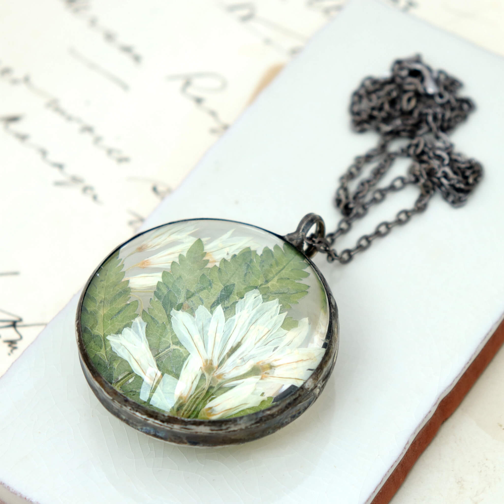 Stained glass style big round pressed flowers necklace lying on a white dish