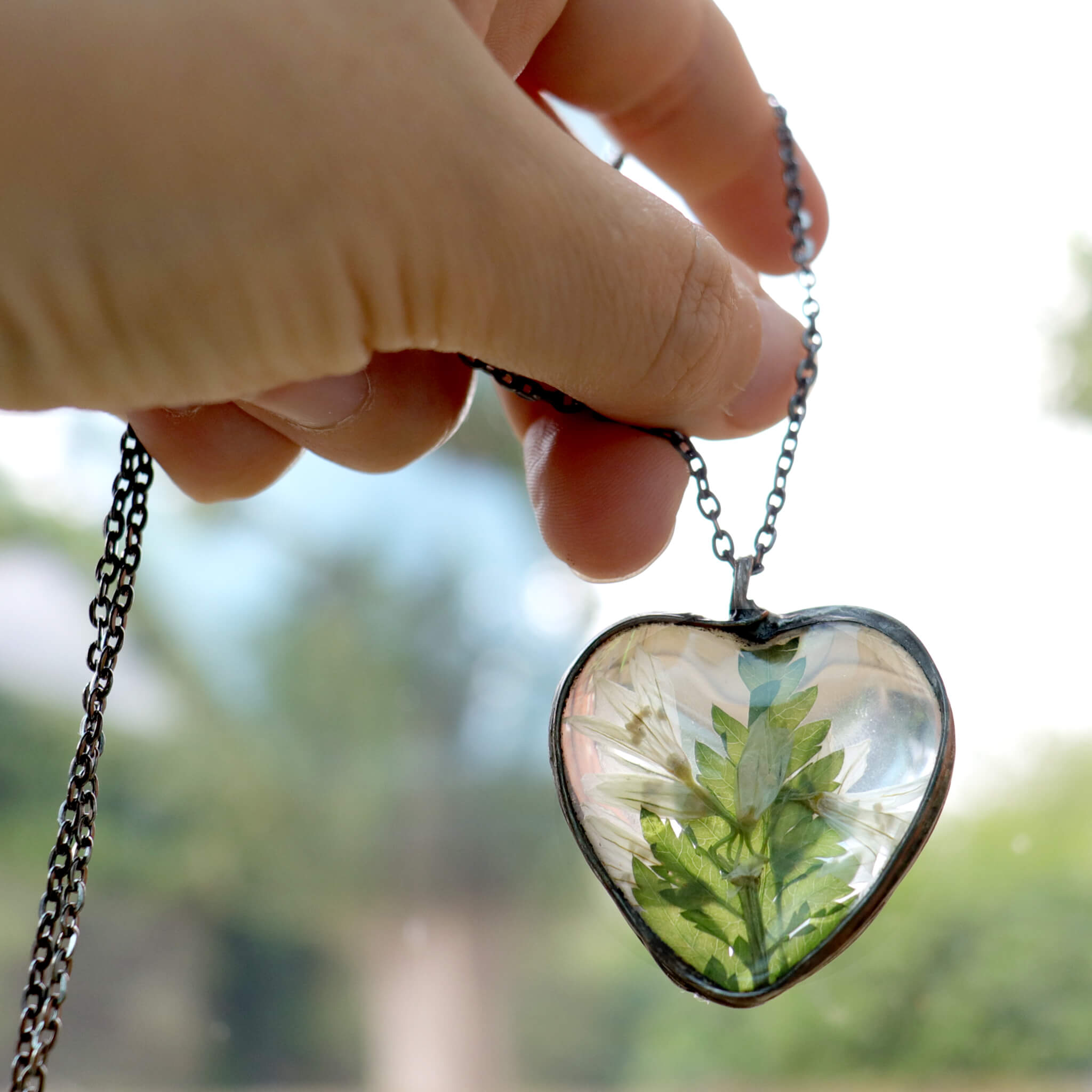 Hand holding Heart shaped necklace with pressed flowers in focus blurry background