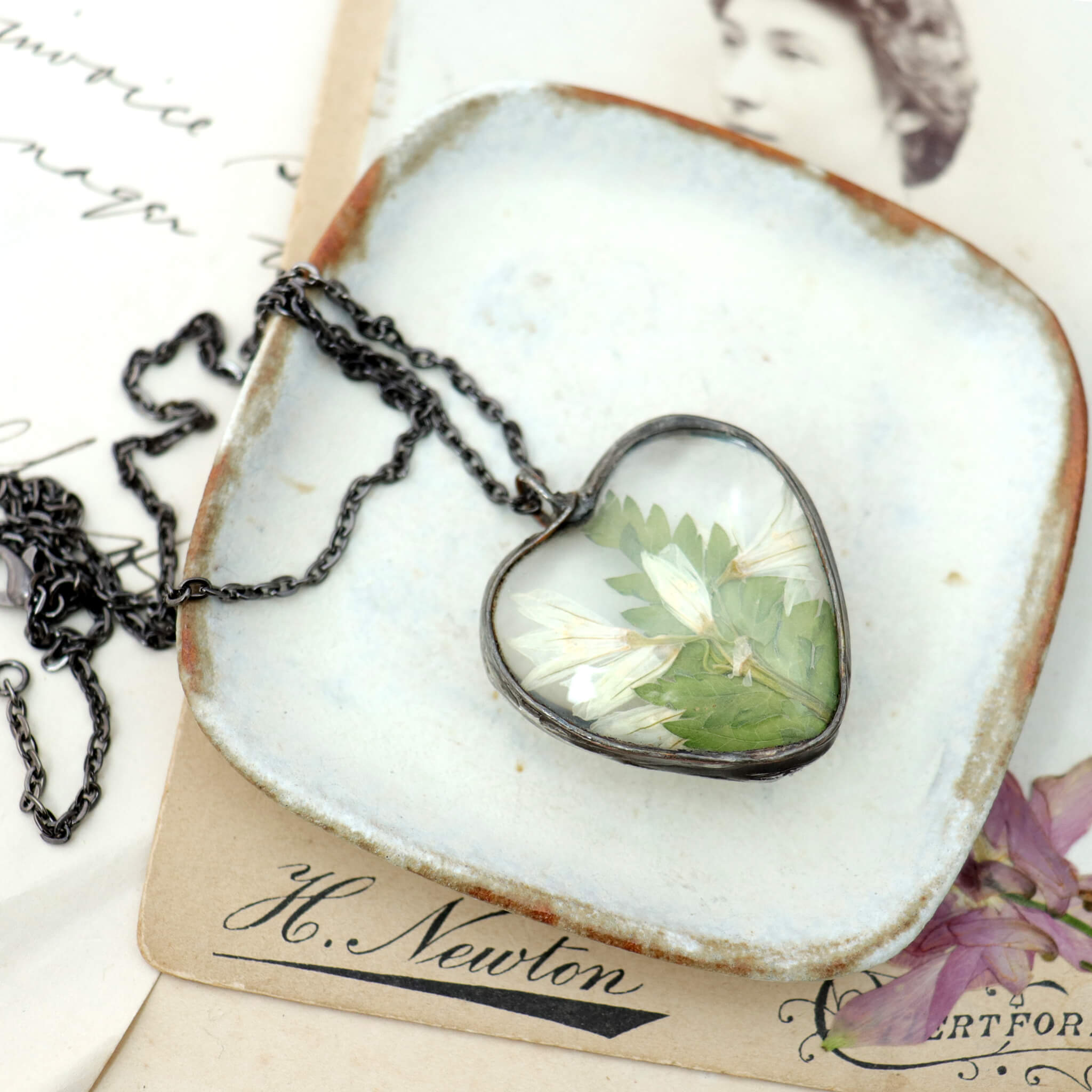 Stained glass style pressed flowers necklace lying on a white dish