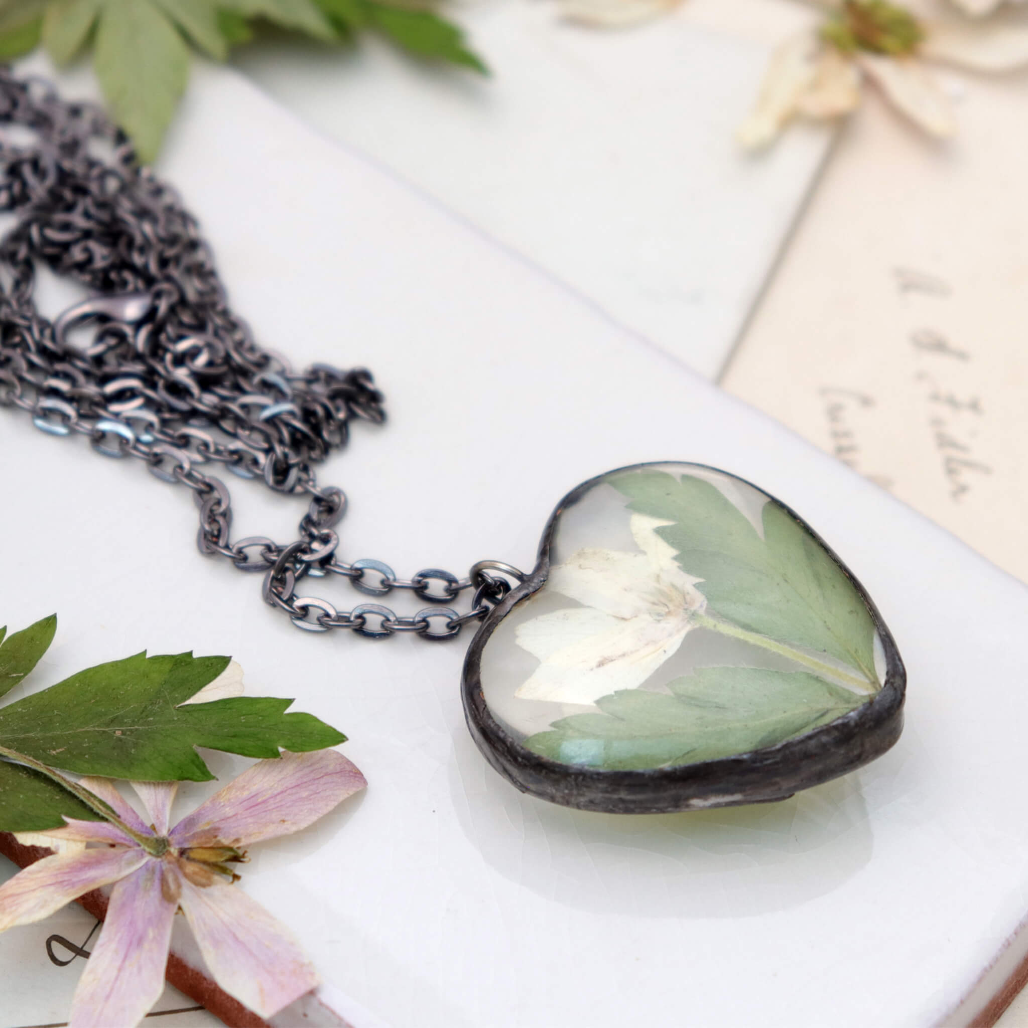 Heart shaped necklace featuring white pressed flowers with green leaves