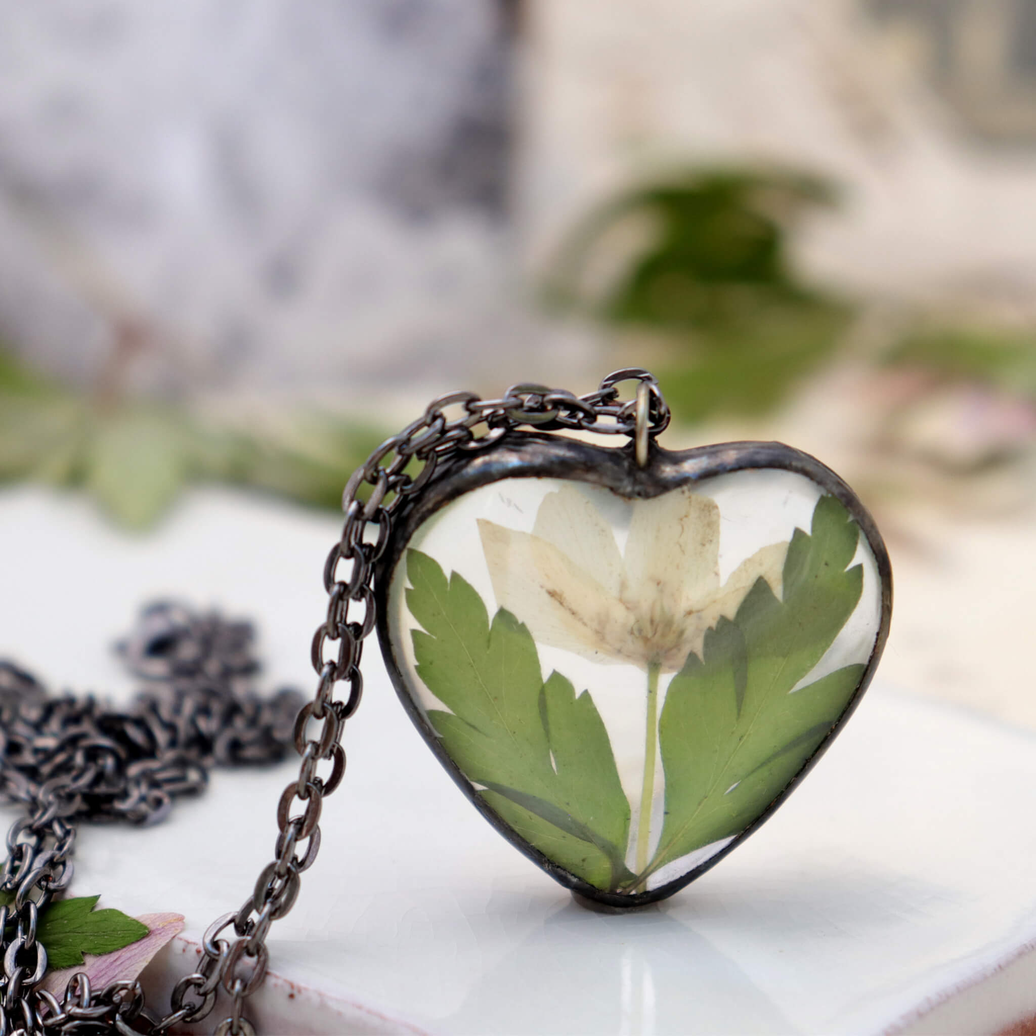Heart shaped necklace featuring white pressed flowers with green leaves