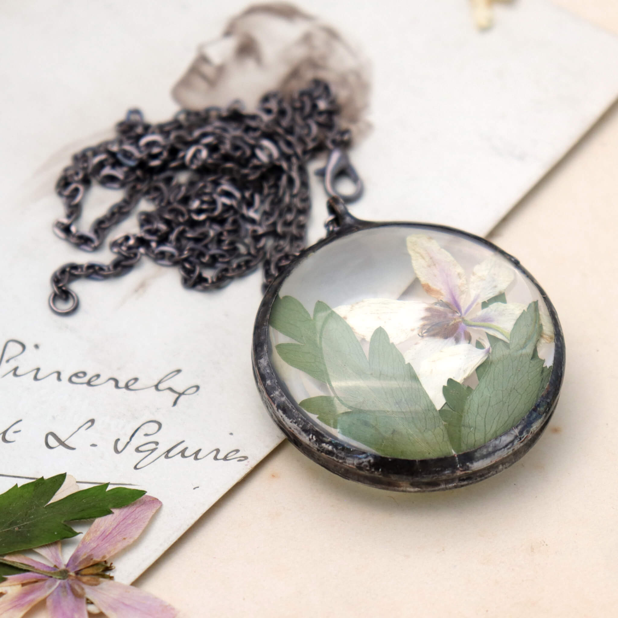 Round shaped necklace featuring white pressed flowers with green leaves