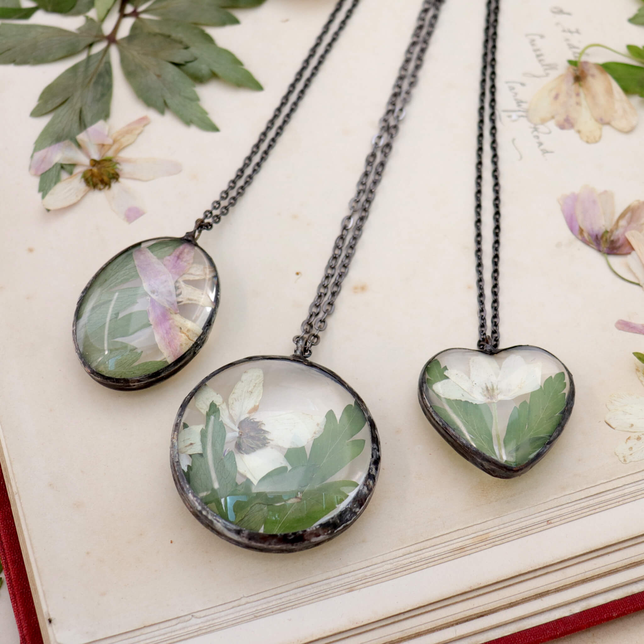 Oval, round and heart shaped necklaces on an old book. Pressed flowers around them