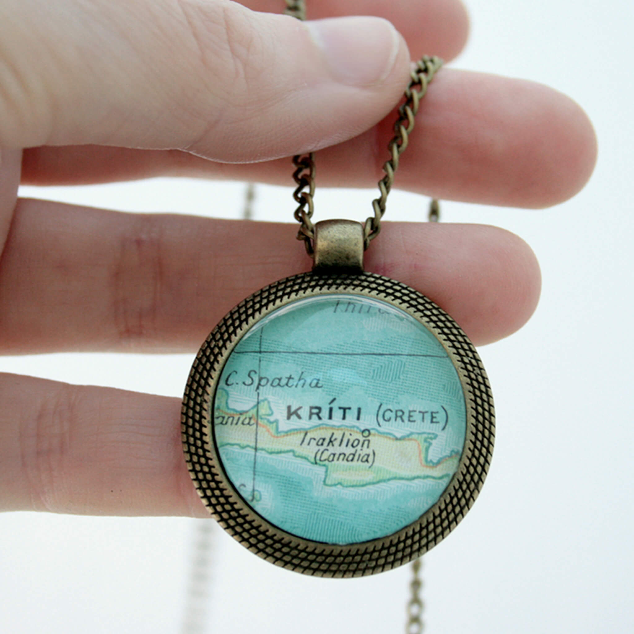 Hand holding bronze coloured pendant necklace with map of Kriti